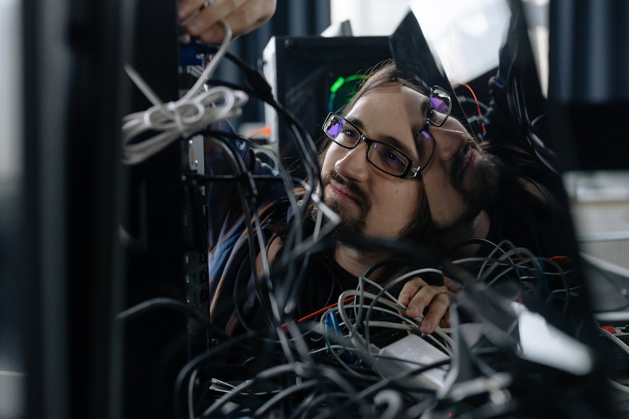 A skilled IT technician organizing tangled cables at his workstation in an office environment.